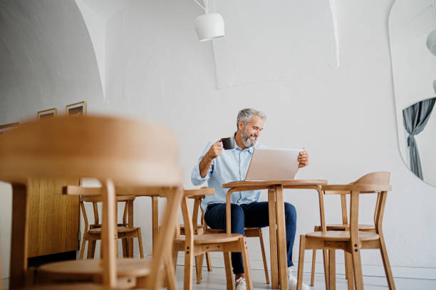 istock Attractive mature man sitting in coffee shop and using laptop computer 1411884521