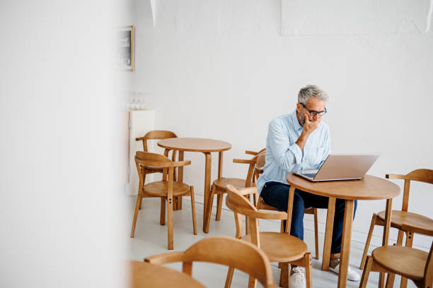 istock Contemplating businessman in the restaurant feeling sad. Full concentration on work. Confident mature man working on laptop while sitting at his working place in office. Tired manager sitting in restaurant surrounded with coffee and laptop computer having 1411886289