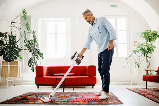 homme de nettoyage de maison avec aspirateur sans fil - carpet caucasian domestic room home interior photos et images de collection