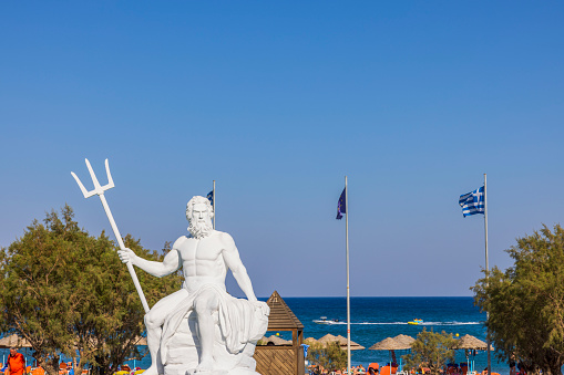 Rhodes. Greece. 07.15.2022.  Beautiful view of Poseidon sculpture on Greek flags and blue sky background.