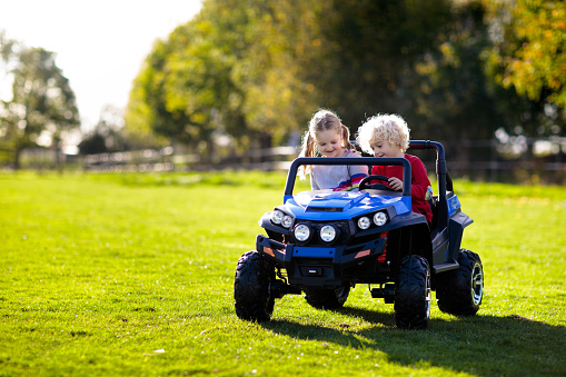 Kids driving electric toy car in summer park. Outdoor toys. Children in battery power vehicle. Little boy and girl riding toy truck in the garden. Family playing in the backyard.