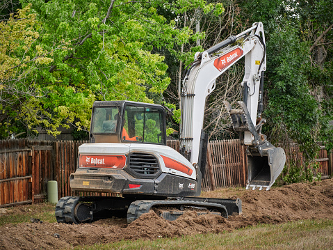 Fort Collins, CO, USA - July 21, 2022: E88, the largest Bobcat compact excavator working in a residential area along backyard fence.
