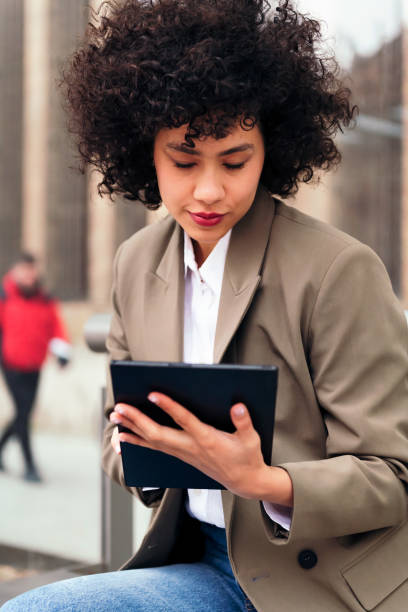 istock young latin woman sitting outdoors using a tablet 1411901891