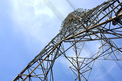low angle view of steel framework of high voltage tower pole with electricity transmission power lines and cloudy blue sky background, infrastructure domestic electric energy industry