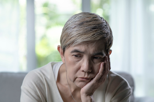 Portrait of middle-aged Asian woman looking troubled worried and depressed about personal health problems and diseases. Retired senior woman disappointed with life feeling lonely, sitting at home waiting for someone. Mature woman looking sad with mental disorders and memory loss alzheimer amnesia.