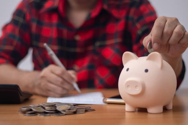 istock Man putting coin in clear plastic jar (Saving concept) 1411918275