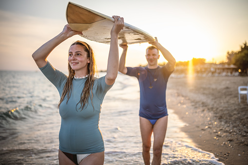 A fit young couple carrying  their surfboard out to the sea and get ready to catch the waves
