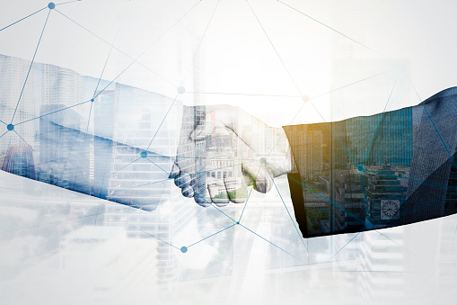 Double exposure of two businessmen handshaking with connection network and cityscape background