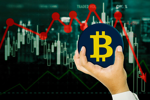 Close up of businessman hand holding a bitcoin with declining price chart background