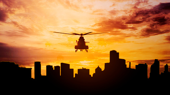 Silhouette of army helicopter hovering over the modern city. Shot at sunset time
