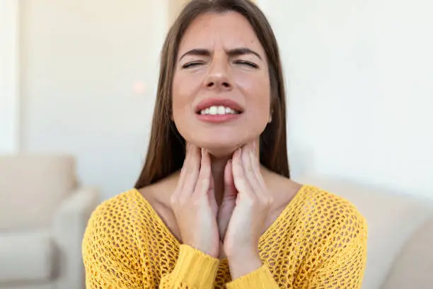 Photo of Close up of young woman rubbing her inflamed tonsils, tonsilitis problem, cropped. Woman with thyroid gland problem, touching her neck, girl has a sore throat