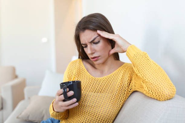 istock Depressed young woman having headache while drinking coffee on sofa at home. 1411934628