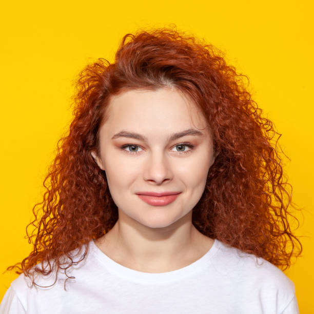 Young woman with red curly hair close-up studio portrait on yellow background stock photo