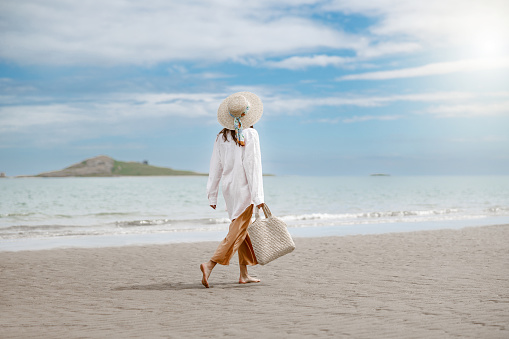 Cheerful young woman traveler with straw hat walking on beach. Summer travel vacation concept