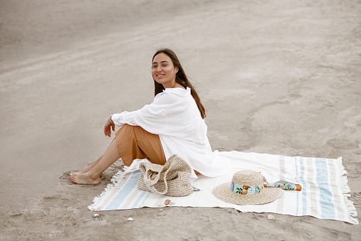 Woman sitting on beach towel near sea and looking camera. Vacation, travel and holiday concept