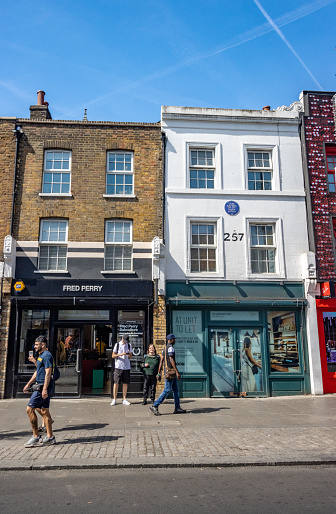 People walking past Tom Sayers Blue Plaque at 257 Camden High Street in Borough of Camden, London. Pugilist Tom Sayers (1826-1865) was a boxing legend of the Victorian era who died at 39.