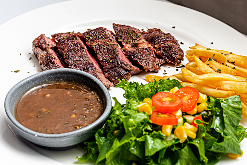A White Plate of Medium Rare Beefsteak served with French Fried and Salad