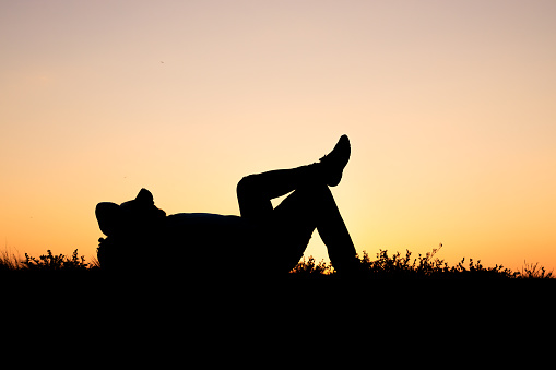 silhouette of resting man on grass on orange background. rest at sunset