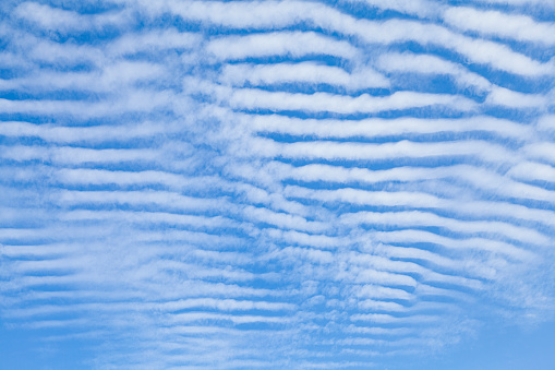 Lines of clouds in the form of lines arranged parallel to each other and framed in such a way that they are arranged horizontally. Blue background with white stripes.