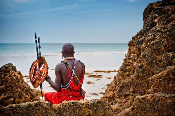 portrait of a Maasai warrior. African man of the Maasai tribe in Kenya sits on the ocean and looks into the distance. The flavor of the journey. Travel Culture warrior person stock pictures, royalty-free photos & images
