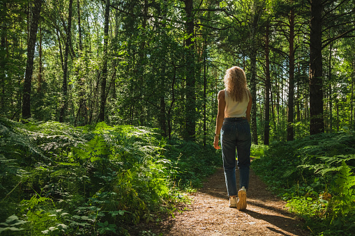 The young woman walks through a dark forest on a sunny day