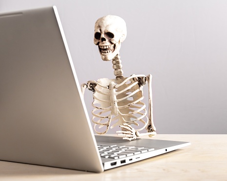 Job burnout. Skeleton sitting at table with laptop. Computer geek. Person suffering from stress at work. Mental and physical exhaustion, fatigue. High quality photo