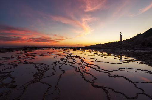 Beautiful sunset with reflections of the clouds and rock formations on Trafalgar beach next to the lighthouse in Cadiz, Andalucia