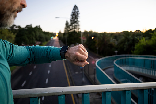 Man running early morning on elevated walkway checking smart watch