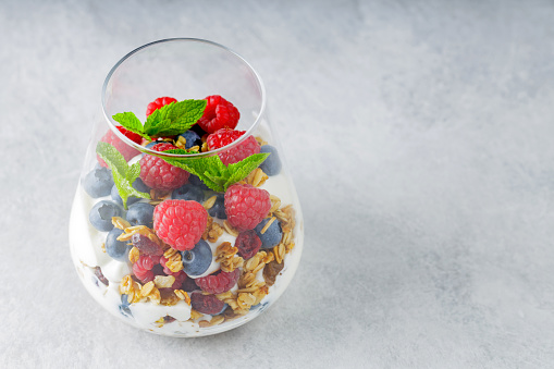 Granola with yogurt and fresh berries served in glass. Jar with puff dessert made of natural yogurt on a gray background. Healthy breakfast concept