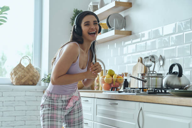 istock Playful young woman using whisk as microphone and smiling while cooking at the kitchen 1411973467