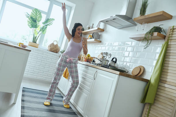 istock Full length of young woman using whisk as microphone while cooking at the kitchen 1411973489