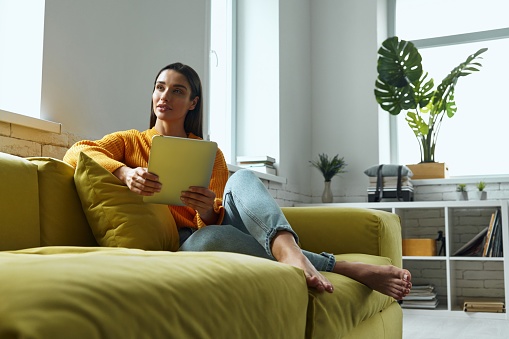 Beautiful young woman using digital tablet while sitting on the couch at home