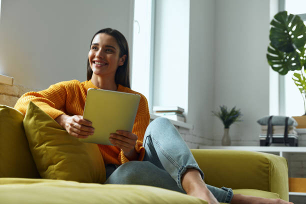istock Attractive young woman using digital tablet and smiling while sitting on the couch at home 1411974584