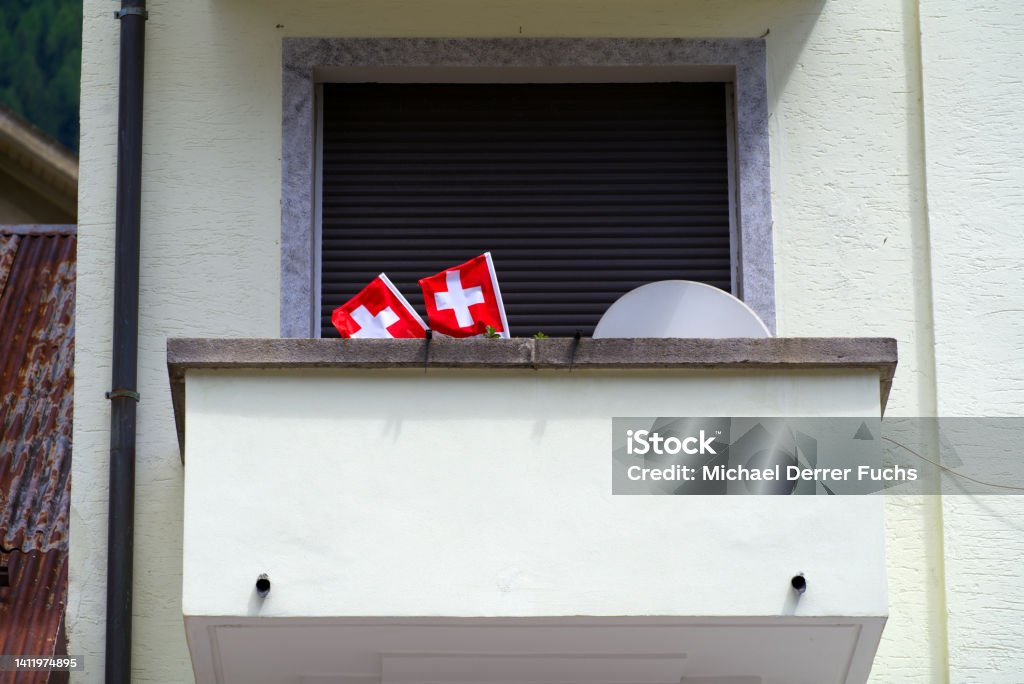 Close-up of balcony with Swiss flags and satellite dish on a sunny summer day. Photo taken June 25th, 2022, Airolo, Switzerland. Airolo Stock Photo