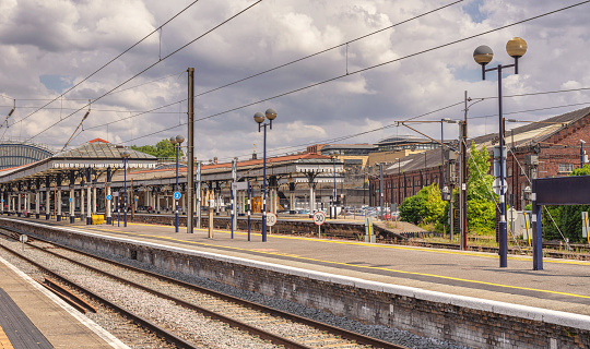York, UK. July 27, 2022.  Historic canopies stand on a railway station platform in the sunshine. Rails are in the foreground and a cloudy sky is above.