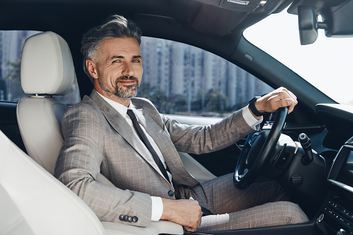 Confident man looking at camera and smiling while sitting on the front seat of a car