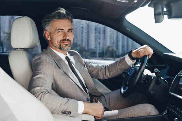 Confident man looking at camera and smiling while sitting on the front seat of a car stock photo