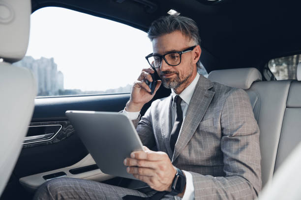 istock Confident businessman using digital tablet and talking on phone while sitting in the car 1411978821