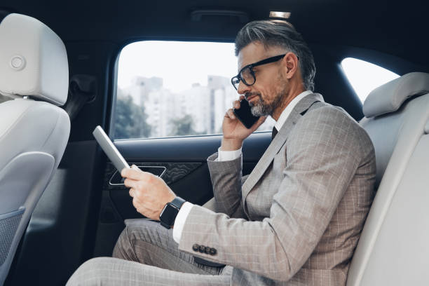 istock Confident mature businessman using digital tablet and talking on phone while sitting in the car 1411978823