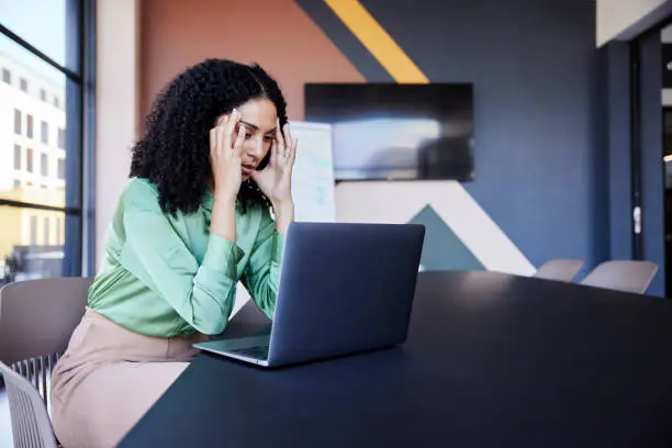 Businesswoman looking stressed out while working on a laptop at a table in the boardroom of an office before a presentation
