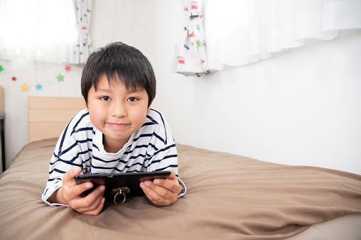 Asian boy looking at tablet device in bed