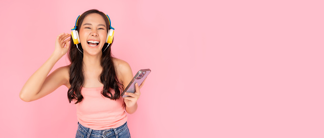 Happy Cheerful woman laughing and enjoy listening music Pretty girl listening music by using headphones and smartphone Young Asian women love listening music with pink background and copy space