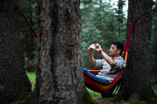 istock Asian middle age man lying in hammock and using smartphone in forest 1411991768