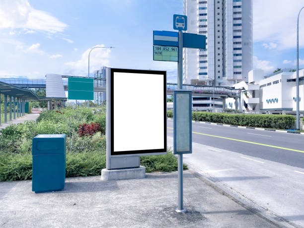 istock Blank vertical advertising poster banner mockup at empty bus stop shelter by main road, greenery behind; out-of-home OOH vertical billboard media display space. 1411992865