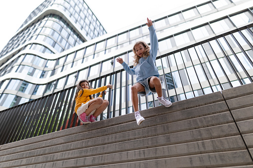 Two girls firends jumping down from concrete wall in city. Low angle view.