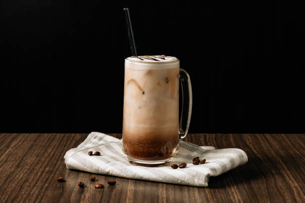 Iced mocha coffee with cream in a tall glass and coffee beans, portafilter, tamper and milk jug on dark wooden background. Cold summer drink. Iced mocha coffee with cream in a tall glass and coffee beans, portafilter, tamper and milk jug on dark wooden background. Cold summer drink. mocha stock pictures, royalty-free photos & images