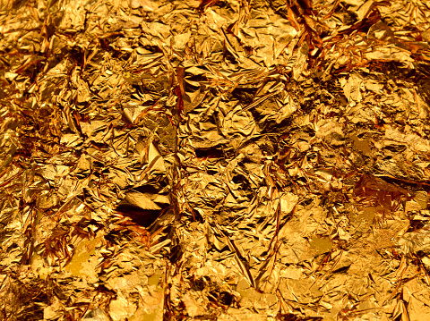 Bangkok, Thailand: wrinkled glittering pure gold leaf / foil texture pattern background - gold leaf applied to a Thai Buddhist temple - thin gold leafing can be purchased as small sheets to be placed on the Buddha statues and other sacred temple elements. In Thai temples numerous figures can be seen covered in gold leaf.