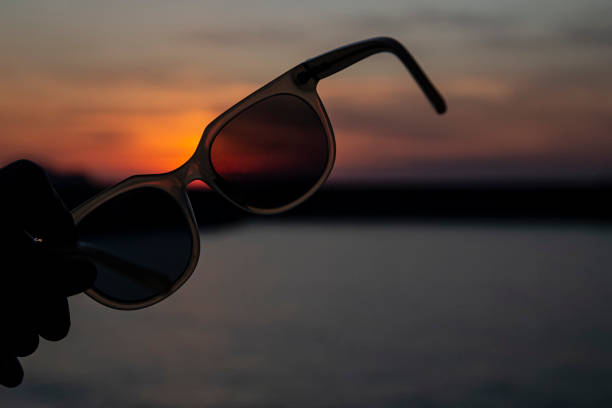 istock Hand holding sunglasses on a beach at sunset 1411996397