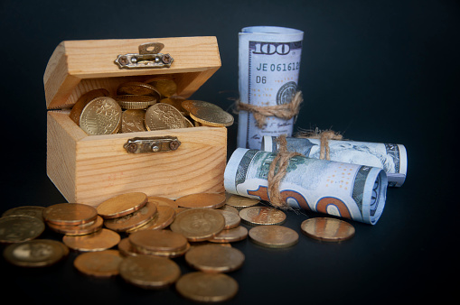 Gold coins in treasure chest and bank notes isolated on dark background cover. Copy space and wealth concept