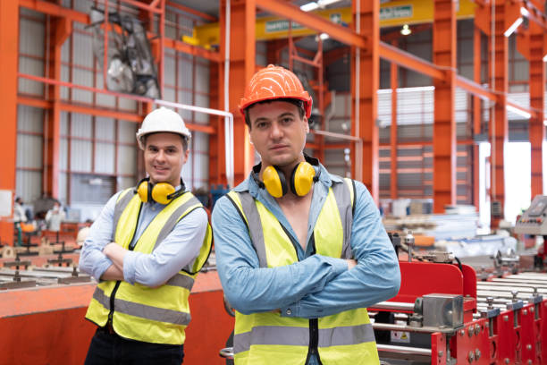 istock Selective focus at Caucasian men mechanical engineer, wearing safety equipment. While doing machine maintenance and safety control inside of factory area. With blurred background of heavy machine. 1411999991